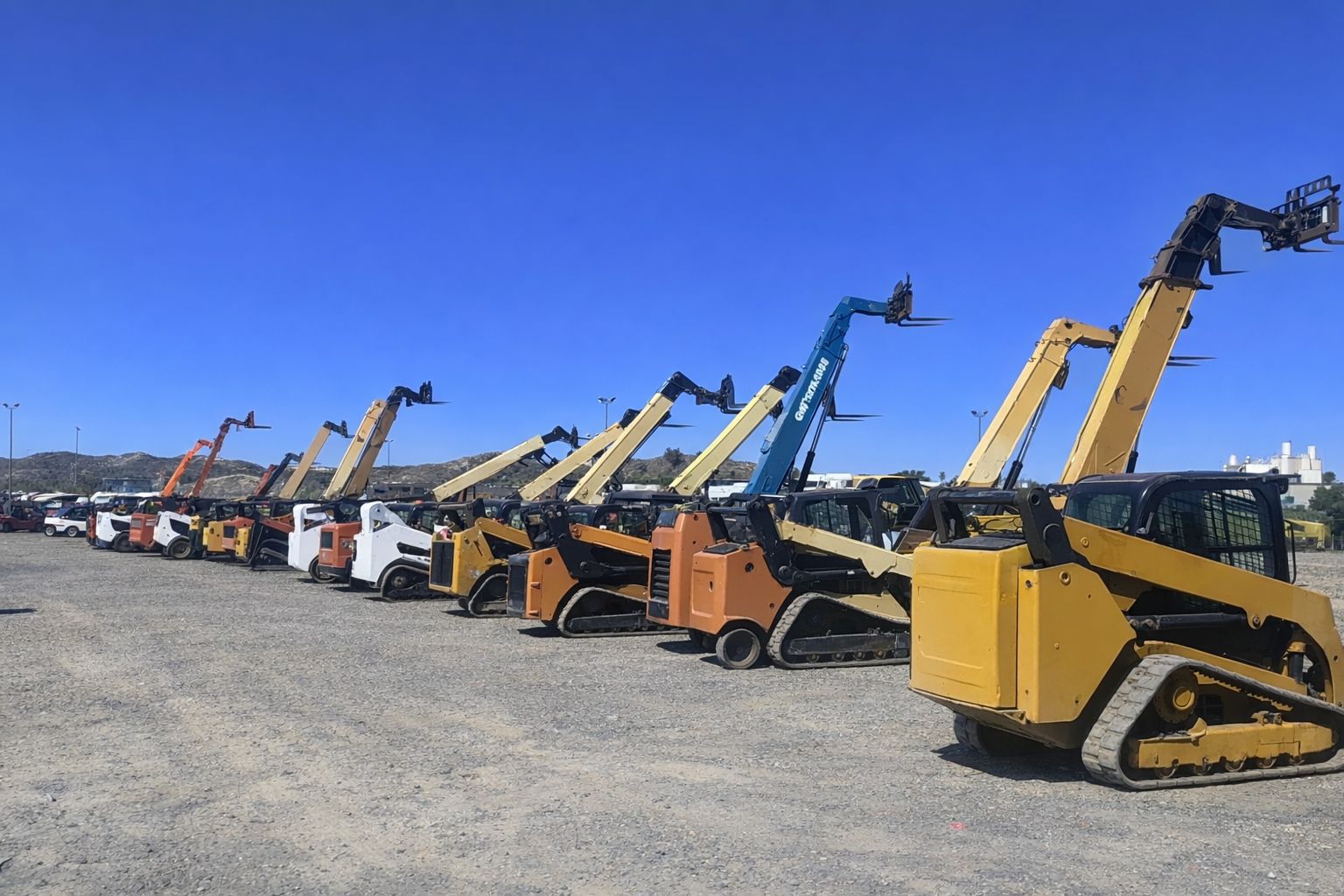 Eine Reihe verschiedener Kompaktlader und Nutzfahrzeuge bei einer Auktion im Freien.